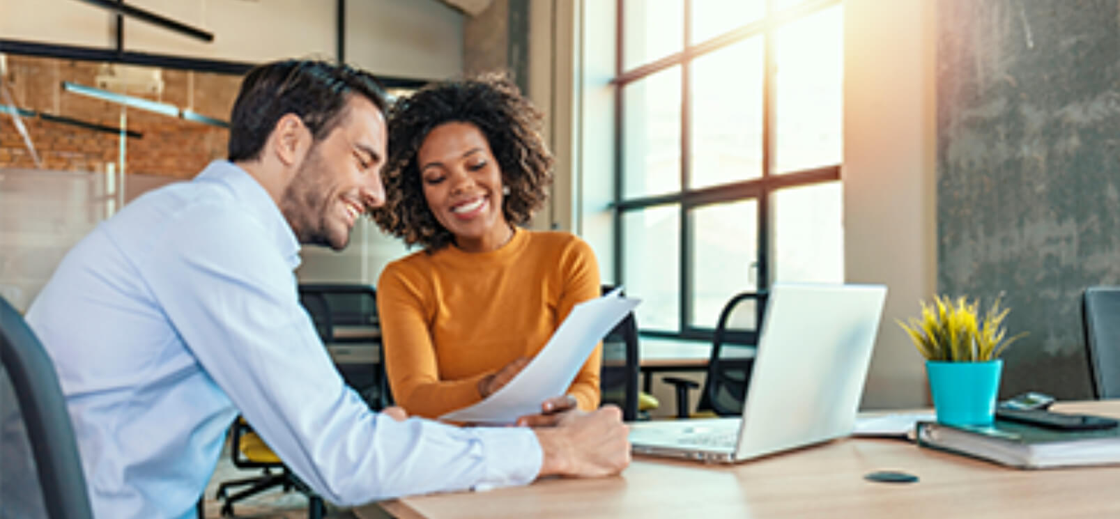 Two people looking at a piece of paper and notebook computer