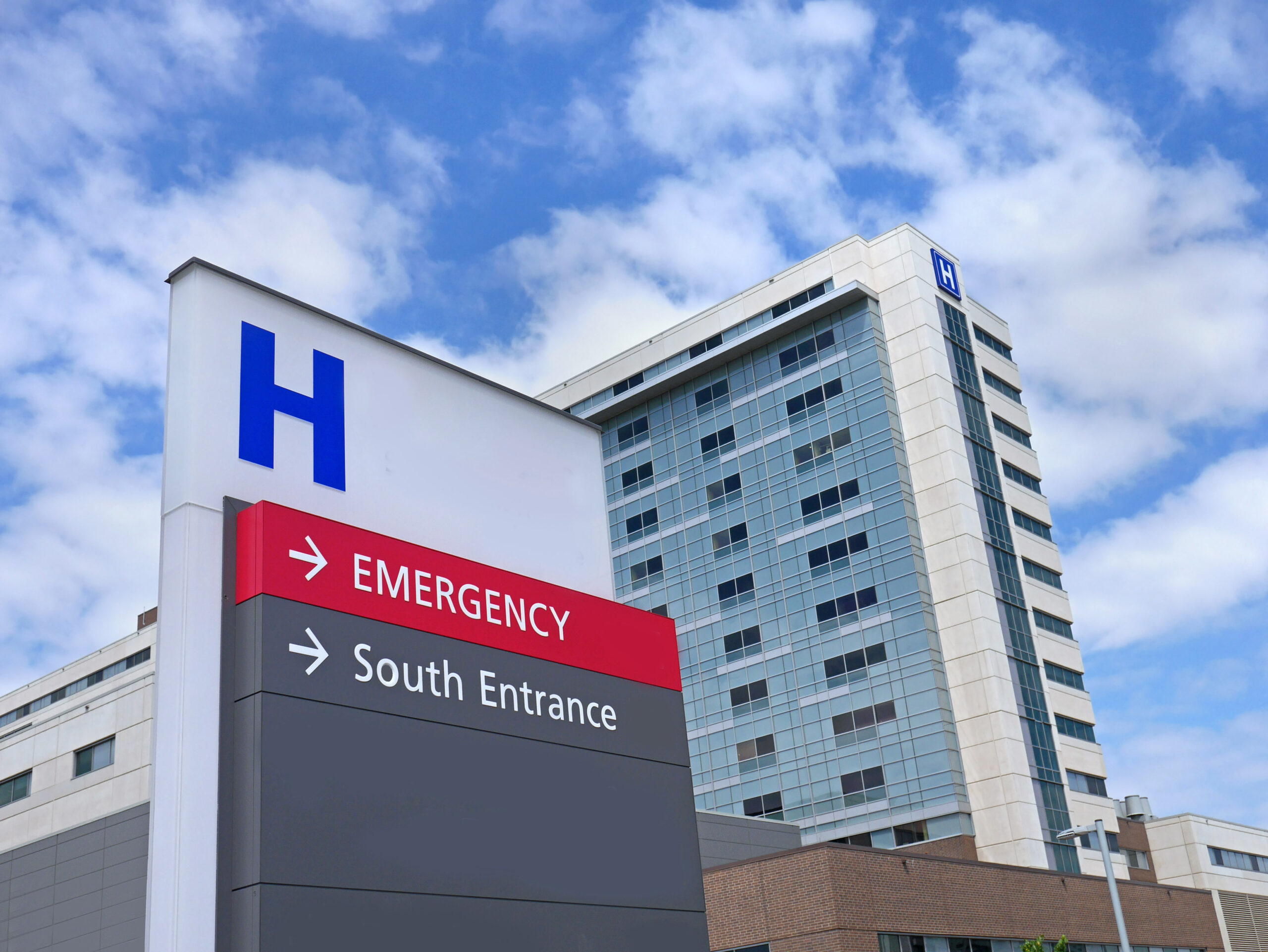 direction sign with capital letter H for with hospital building in the background